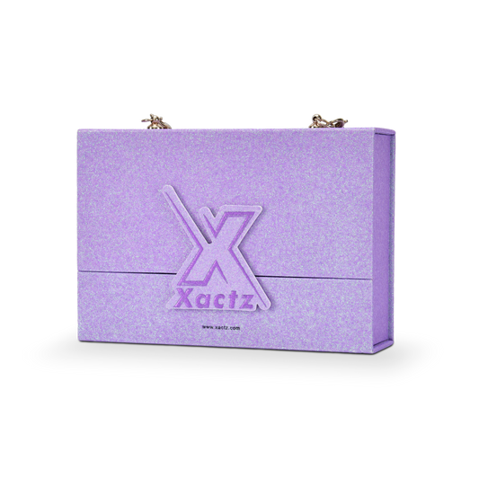 Three quarter angled view of a custom purple glitter rigid makeup gift box with luxury chain handle displaying the full iridescent purple glitter surface wrapping all panels with the embossed purple gold foil Xactz logo on the front and gold chain attachment hardware clips at the top
