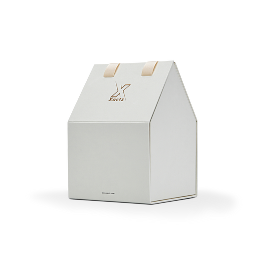 Three quarter angled view of a custom house shaped foldable packaging box displaying its unique architectural roof structure and clean cream white paper finish with a gold foil logo