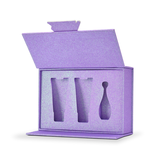 Custom purple glitter rigid makeup gift box with luxury packaging shown open at a three quarter angle revealing the matching purple glitter foam insert interior with three precision cut product cavities holding two cosmetic tubes and one perfume bottle shaped product all surrounded by the continuous iridescent purple glitter surface