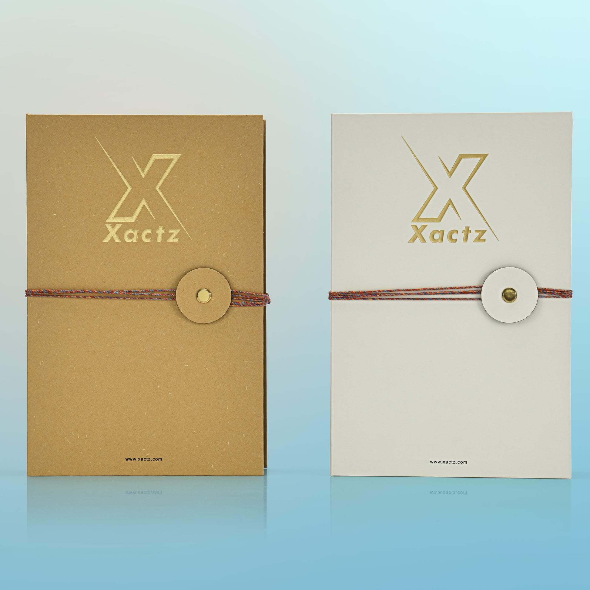 Two custom rigid book style perfume gift boxes standing side by side showing the natural ochre yellow paper variant and the minimalist light grey specialty paper variant both with gold foil logos and rope closures