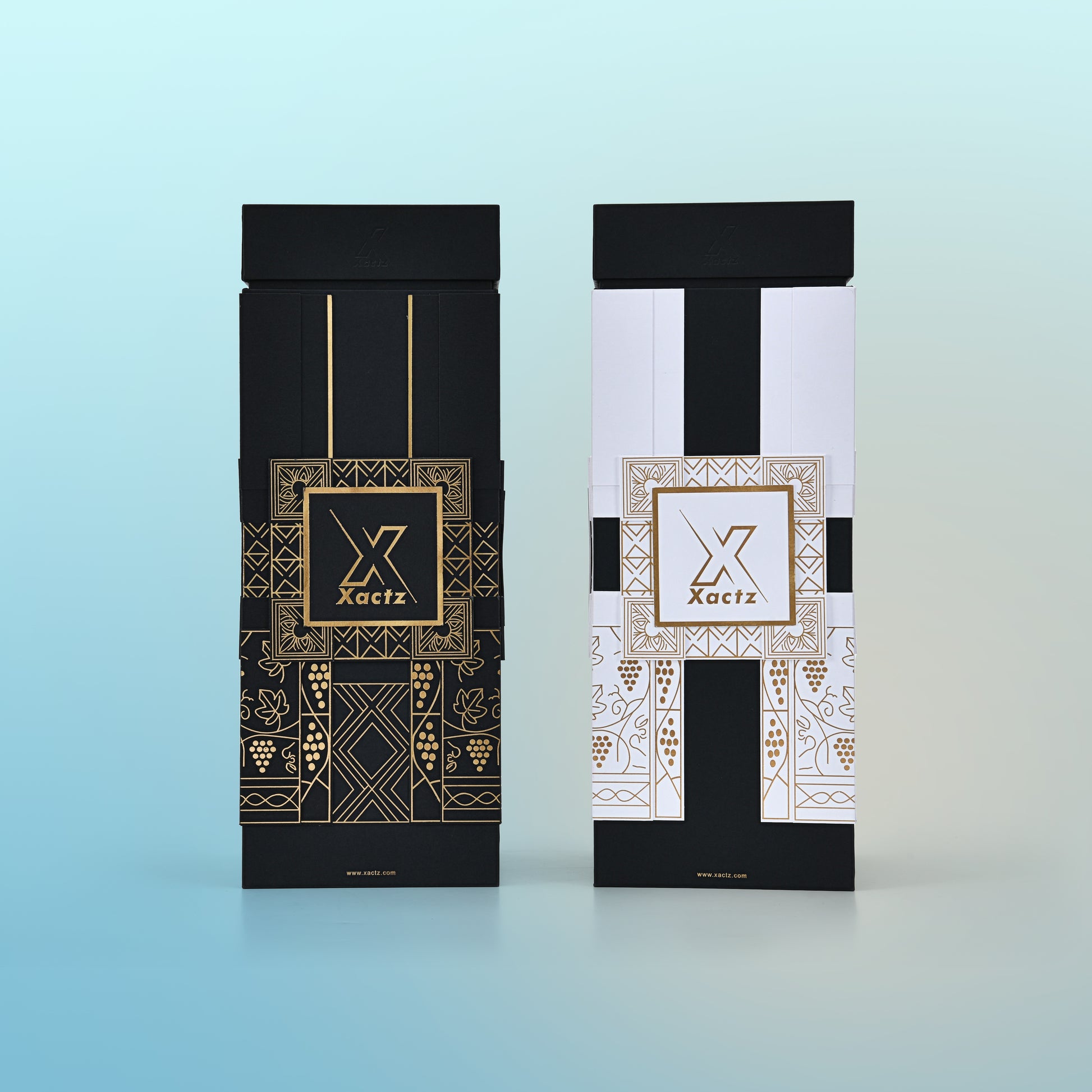 Front view comparison of two custom rigid wine gift boxes side by side showing the all black body version with gold foil grape vine and geometric illustration on the left and the white and black body version with the same gold foil pattern on the right both with matte black collared lids