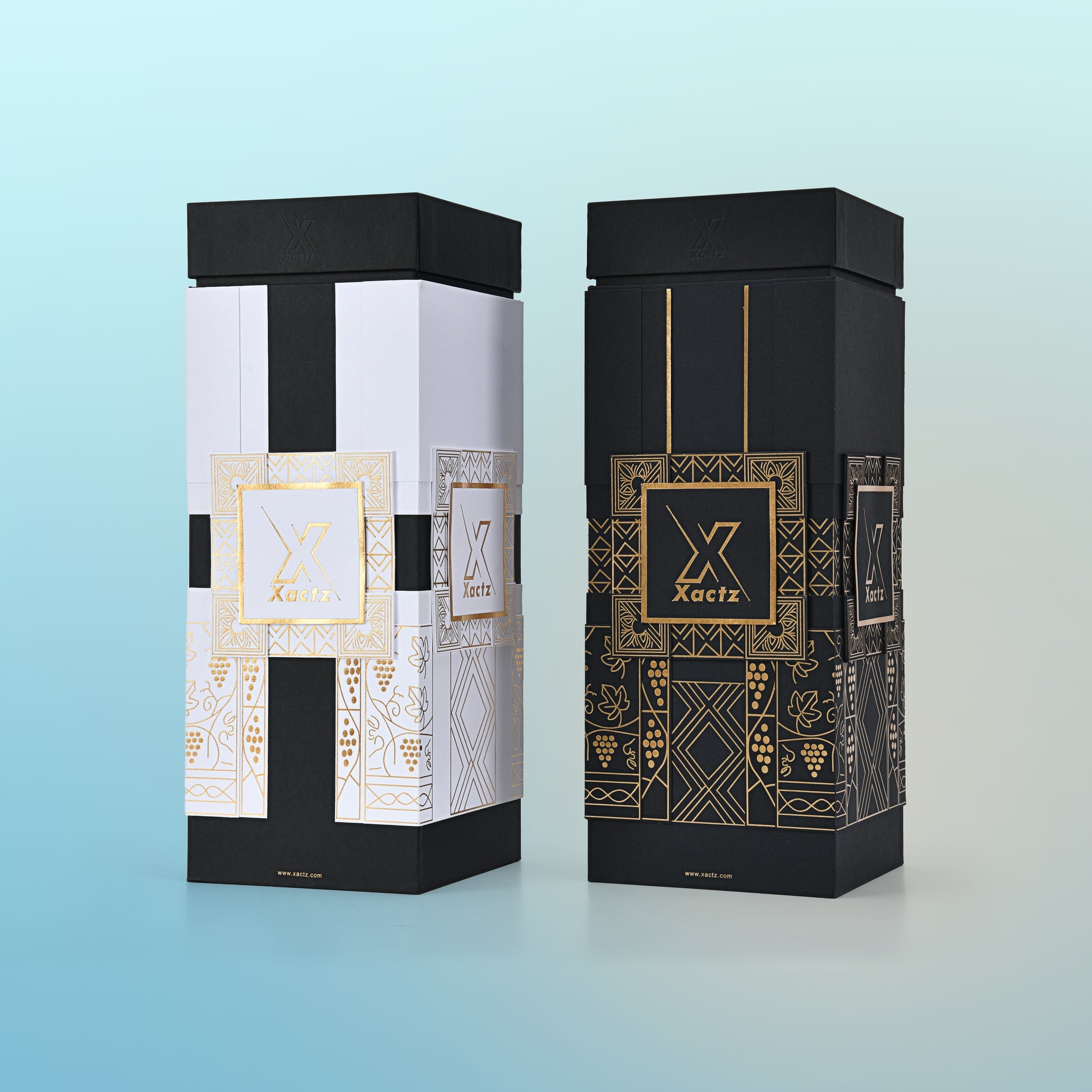 Lifestyle view of two custom black rigid wine gift boxes showing the white and gold foil version standing upright with the matte black lid on and the all black gold foil version placed horizontally beside it displaying the full decorative panel design and collared lid and base construction