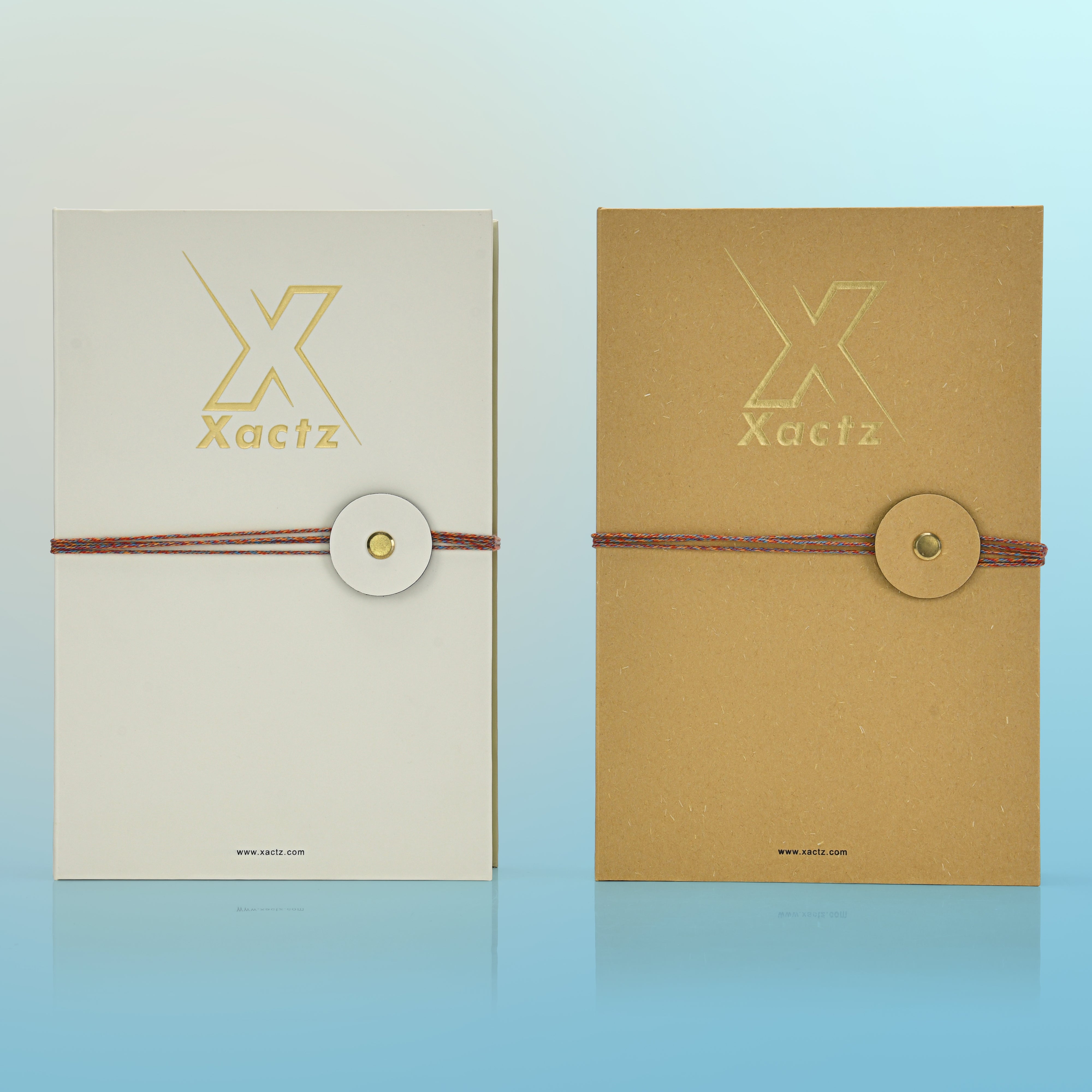 Luxury cream and kraft book style perfume gift box front view comparison showing embossed gold foil Xactz logo and multicolour rope closure with gold metal rivet on both soft-touch laminated cream and natural kraft variants